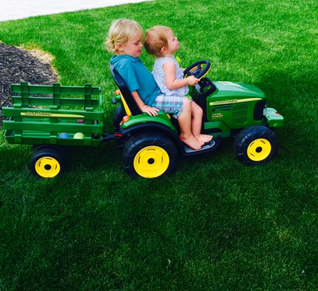 two kids playing on toy tractor in backyard