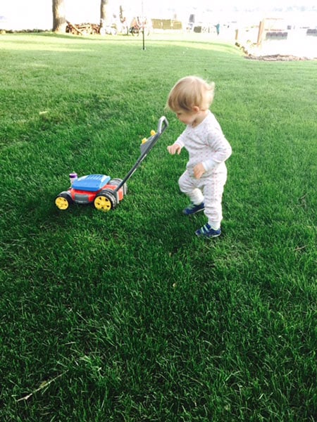 young child playing with toy lawn mower on grass