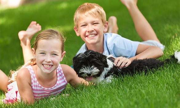 two kids and a dog laying on grass smiling